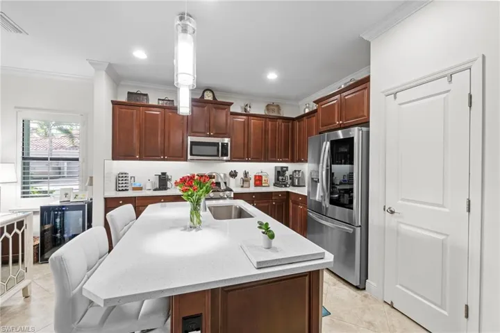 The kitchen features rich wood cabinetry, stainless steel appliances, a spacious island with a sink, and a light-colored countertop