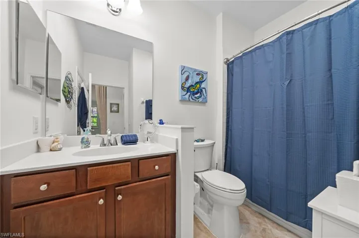 Bathroom featuring a vanity with a white countertop and wood cabinetry, a large mirror, and a shower with a blue curtain