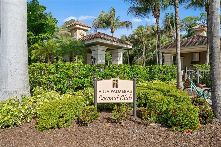 The property entrance features a sign for "Villa Palmeras Coconut Club" surrounded by well-maintained landscaping, including various shrubs and palm trees