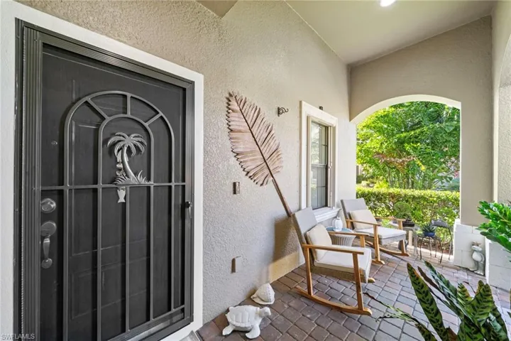 The property features an inviting entryway with a decorative security door, a covered porch with a brick-patterned floor, and an arched opening looking out to lush greenery