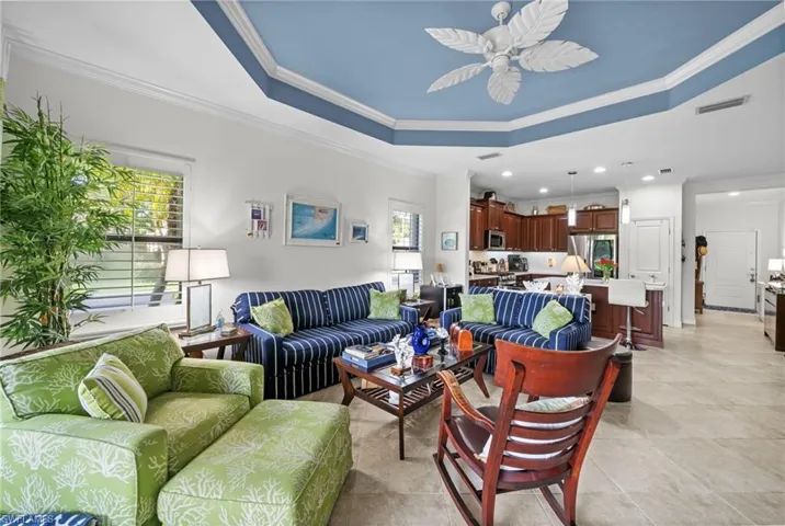 The open concept living area features a decorative tray ceiling with a ceiling fan, tiled flooring, and a kitchen with wooden cabinetry