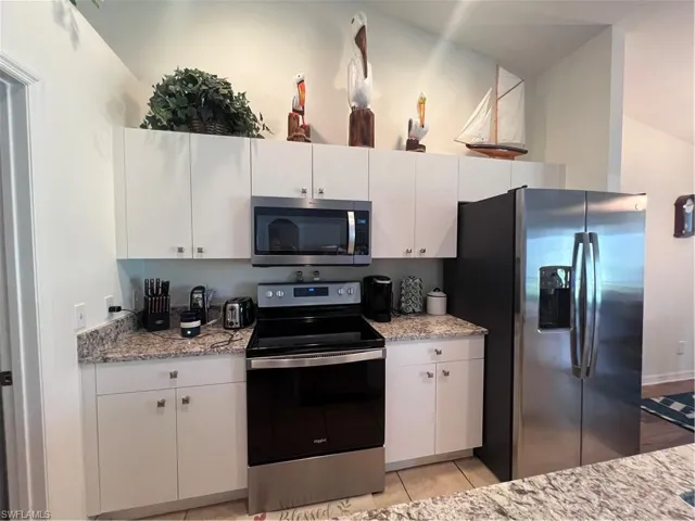 Kitchen with range, light stone counters, fridge, and white cabinets