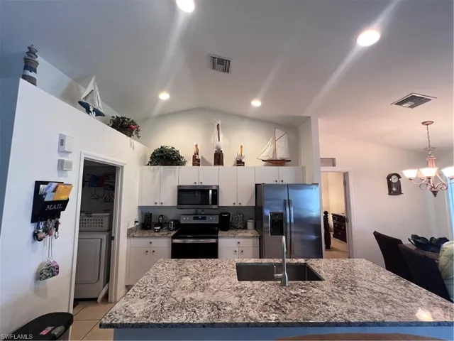Kitchen featuring stove, sink, white cabinetry, fridge, and vaulted ceiling