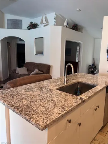 Kitchen featuring light tile patterned flooring, light stone counters, vaulted ceiling, and sink