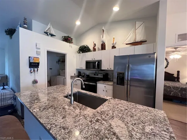 Kitchen featuring lofted ceiling, sink, white cabinetry, washer and clothes dryer, and stainless steel appliances