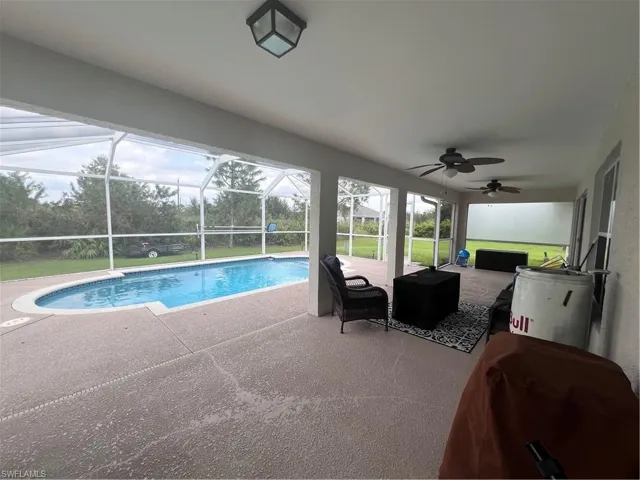 View of pool featuring glass enclosure, a patio area, and ceiling fan
