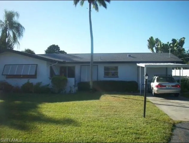 Ranch-style house featuring concrete driveway, a carport, a front yard, stucco siding and large storm windows and shutters