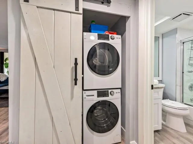 Laundry area with a barn door, light wood-type flooring, and stacked washer and clothes dryer