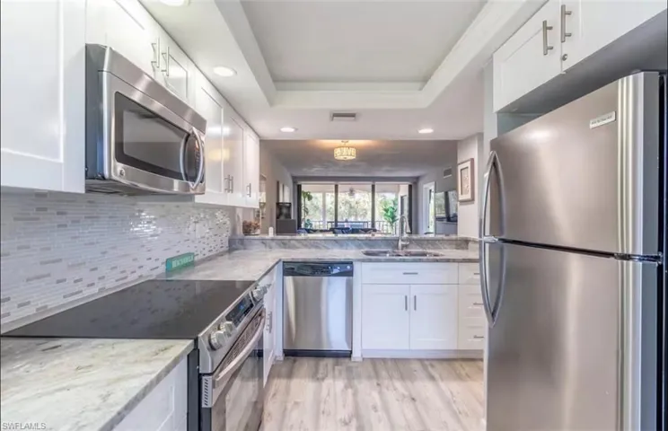Kitchen featuring stainless steel appliances, white cabinetry, recessed lighting, light stone countertops, and light wood-type flooring