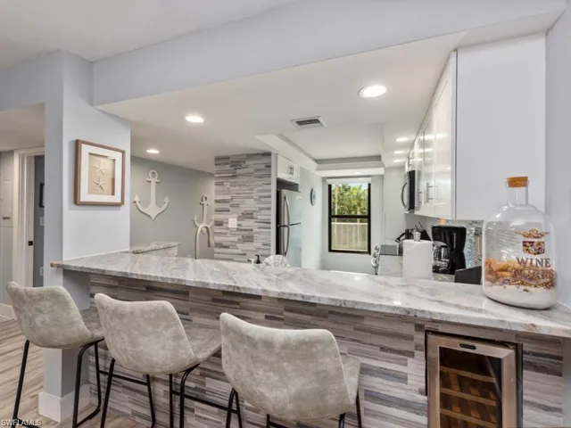 Indoor wet bar with light stone countertops, stainless steel appliances, white cabinetry, light wood-type flooring, and recessed lighting