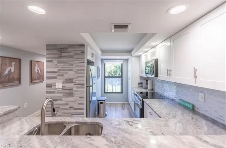 Kitchen with stainless steel appliances, light stone countertops, white cabinets, light wood-style floors, and a tray ceiling