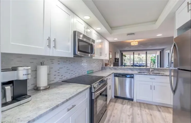 Kitchen featuring stainless steel appliances, recessed lighting, white cabinets, light stone counters, and light wood finished floors