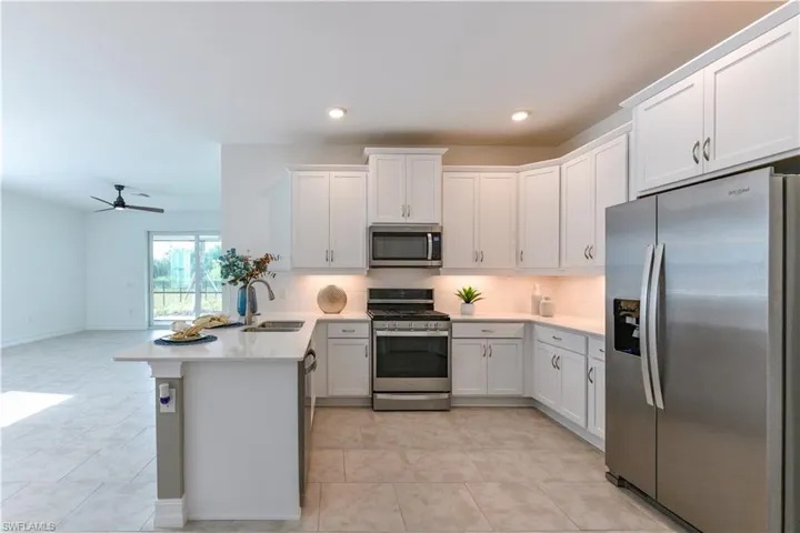 Kitchen with stainless steel appliances, backsplash, a peninsula, open floor plan, and white cabinets