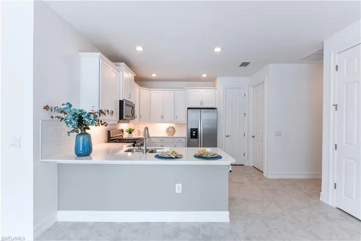 Kitchen with decorative backsplash, appliances with stainless steel finishes, white cabinets, a peninsula, and recessed lighting