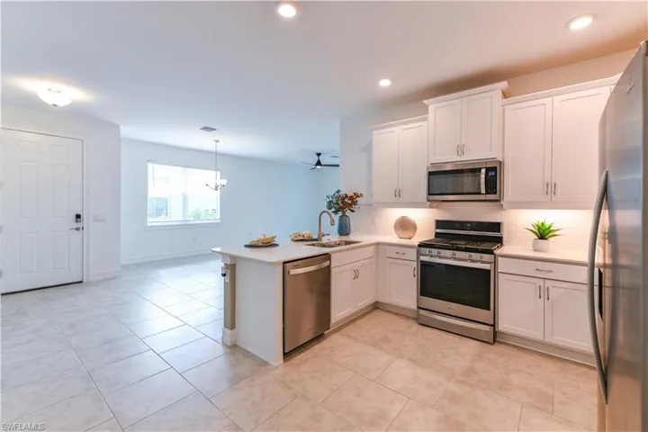 Kitchen featuring appliances with stainless steel finishes, white cabinets, a peninsula, backsplash, and pendant lighting