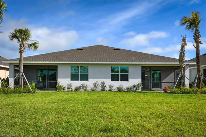 Back of property featuring a sunroom, stucco siding, a lawn, and a shingled roof