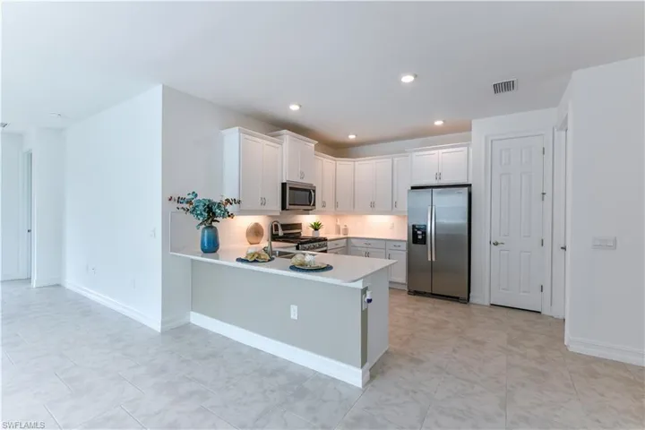 Kitchen featuring appliances with stainless steel finishes, a peninsula, backsplash, white cabinetry, and recessed lighting