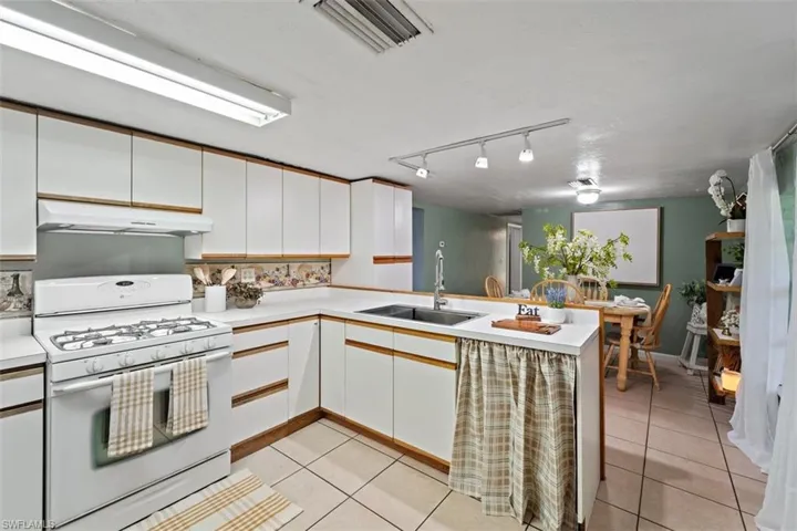 Kitchen with light tile patterned floors, sink, white cabinets, kitchen peninsula, and white gas stove