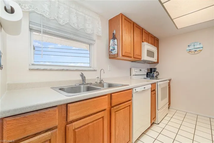 Kitchen featuring light wood cabinetry, a dual basin stainless steel sink, white countertop, and white tile flooring
