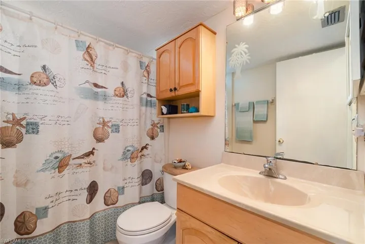Bathroom featuring a vanity with an integrated sink, a large wall-mounted mirror, and a wall-mounted wood-finish cabinet with open shelving