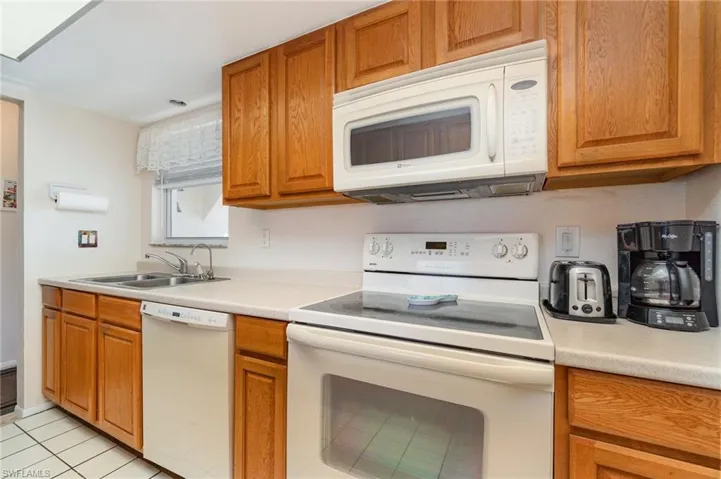 Kitchen featuring wood cabinetry, light-toned countertops, a stainless steel double basin sink, an electric range, and an over-the-range microwave