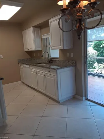 Kitchen with light tile patterned flooring, white cabinetry, dishwashing machine, and an inviting chandelier