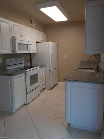 Kitchen with range, sink, white cabinetry, and light tile patterned flooring