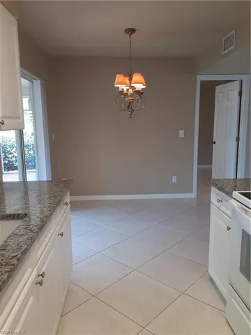 Kitchen featuring a notable chandelier, pendant lighting, light tile patterned floors, and white cabinets