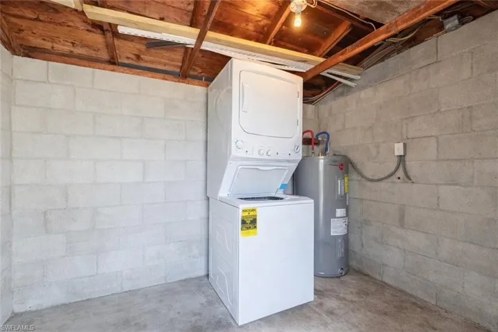 Laundry area featuring stacked washing machine and dryer, water heater, and concrete flooring