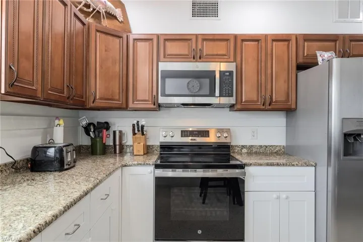 Kitchen with appliances with stainless steel finishes, brown cabinetry, and light stone countertops