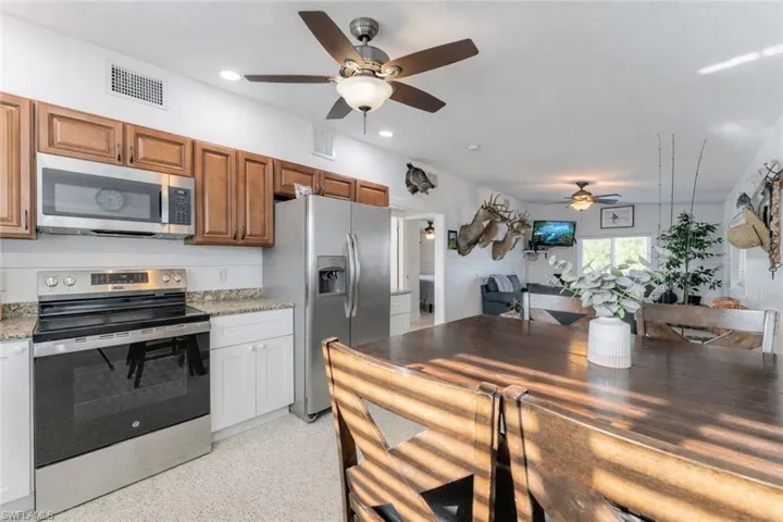 Kitchen with stainless steel appliances, ceiling fan, light stone countertops, dark speckled floor, and recessed lighting