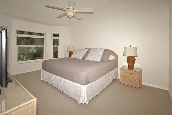 Primary bedroom with newly carpeted flooring,  ceiling fan and vaulted ceiling