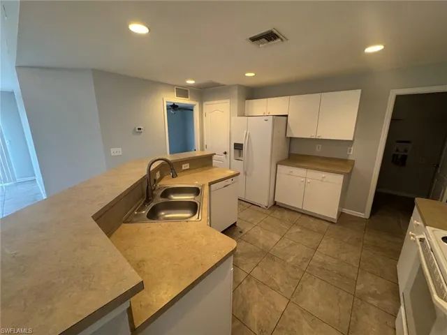 Kitchen featuring white cabinetry, white appliances, light countertops, a large island with sink, and recessed lighting