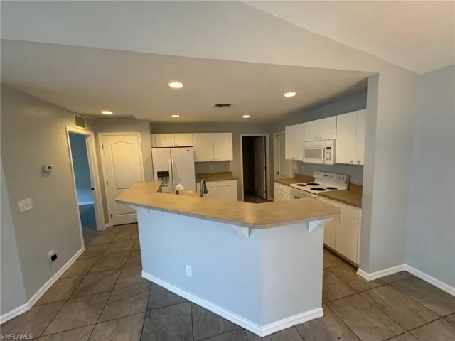 Kitchen featuring white cabinets, a kitchen breakfast bar, white appliances, light countertops, and dark tile patterned flooring