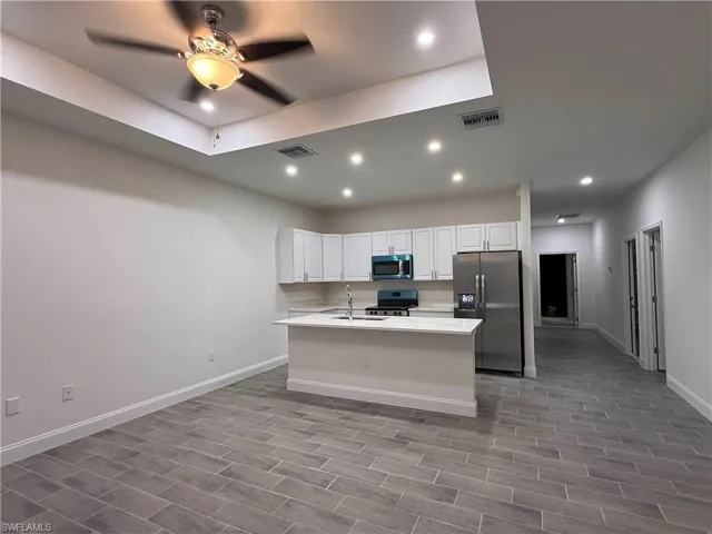 Kitchen with stainless steel appliances, recessed lighting, white cabinets, a center island with sink, and wood finish floors