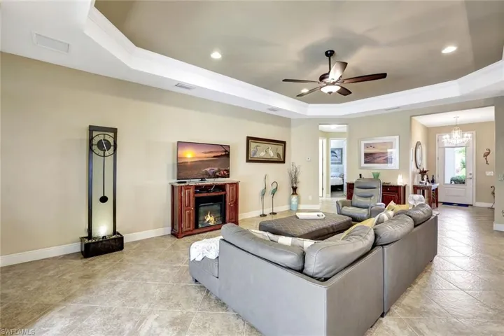 Living area featuring baseboards, visible vents, a raised ceiling, and a glass covered fireplace