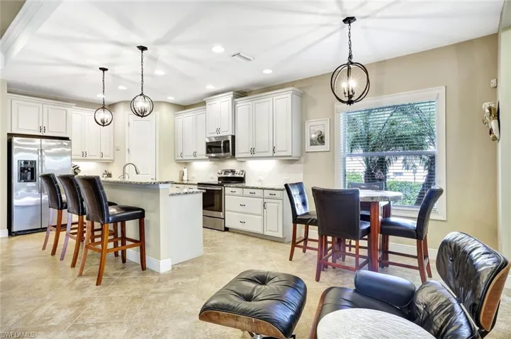 Kitchen featuring tasteful backsplash, white cabinets, light stone counters, a kitchen breakfast bar, and stainless steel appliances