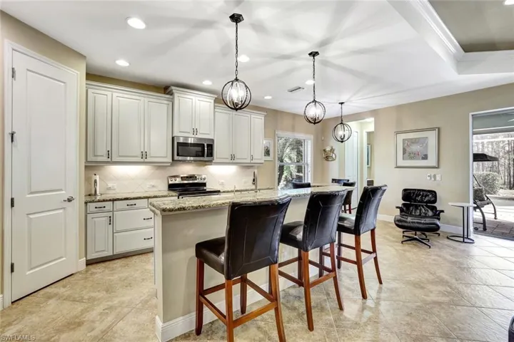 Kitchen with an island with sink, appliances with stainless steel finishes, a kitchen breakfast bar, light stone countertops, and backsplash