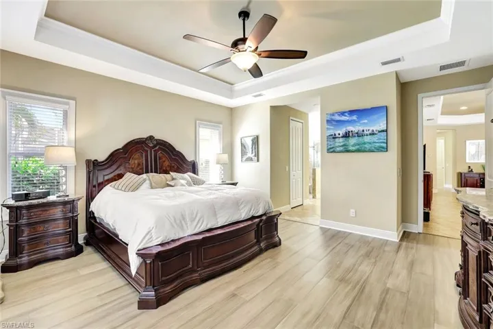 Bedroom featuring light wood-style floors, a tray ceiling, visible vents, and baseboards