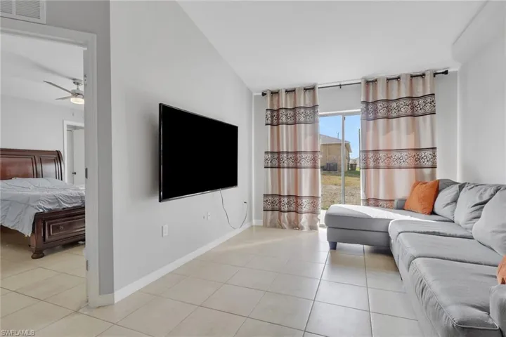 Living room featuring vaulted ceiling, light tile patterned flooring, and a ceiling fan