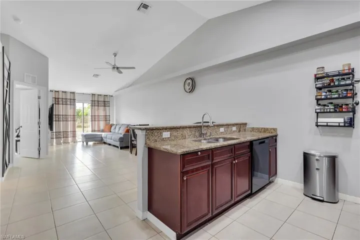 Kitchen featuring bold wood finish cabinetry, a ceiling fan, light stone countertops, lofted ceiling, and open floor plan