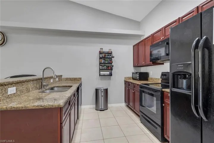 Kitchen with bold wood finish cabinetry, black appliances, light stone counters, a peninsula, and light tile patterned floors