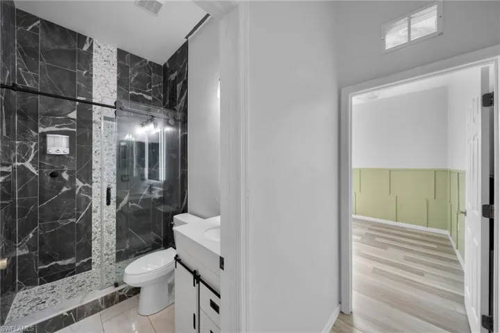 Full bath with a marble finish shower, toilet, and vanity