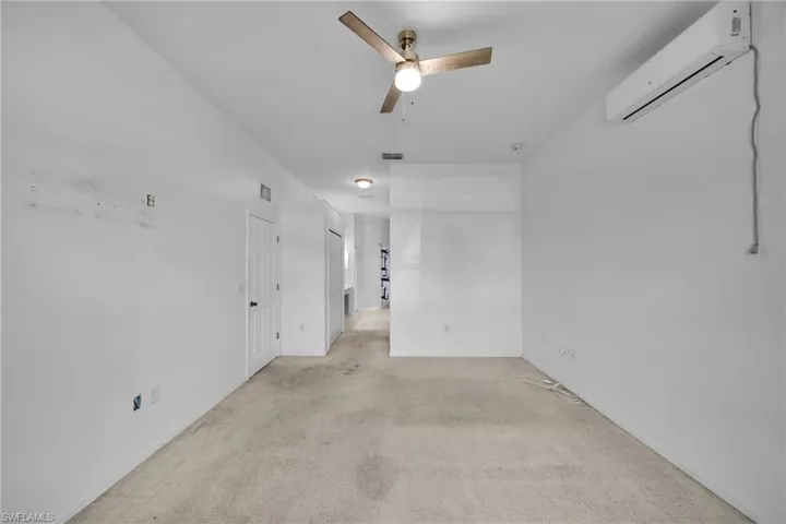Empty room with an AC wall unit, a ceiling fan, and light colored carpet