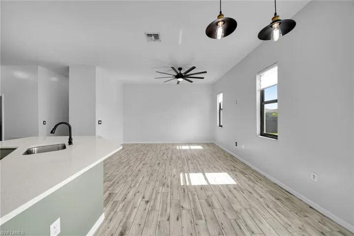 Unfurnished living room with a sink, light wood finished floors, baseboards, and a ceiling fan