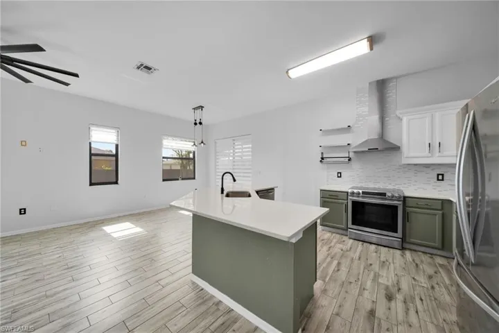 Kitchen with appliances with stainless steel finishes, wall chimney exhaust hood, light countertops, green cabinetry, and light wood-style flooring