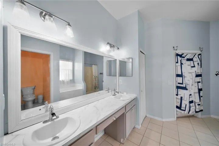 Full bath with toilet, double vanity, tile patterned floors, baseboards, and curtained shower