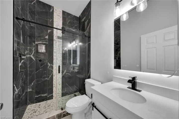 Bathroom with a marble finish shower, vanity, and toilet