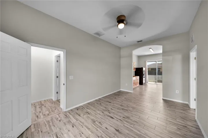 Empty room with arched walkways, ceiling fan, light wood-style floors, and baseboards