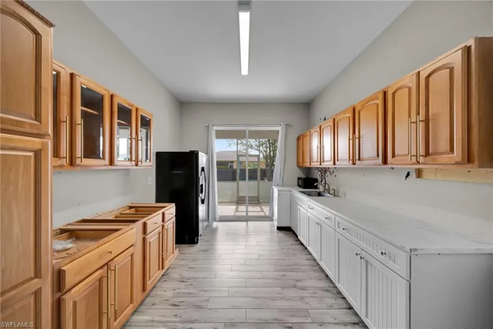 Kitchen with black fridge, glass insert cabinets, a sink, light wood finished floors, and light stone counters